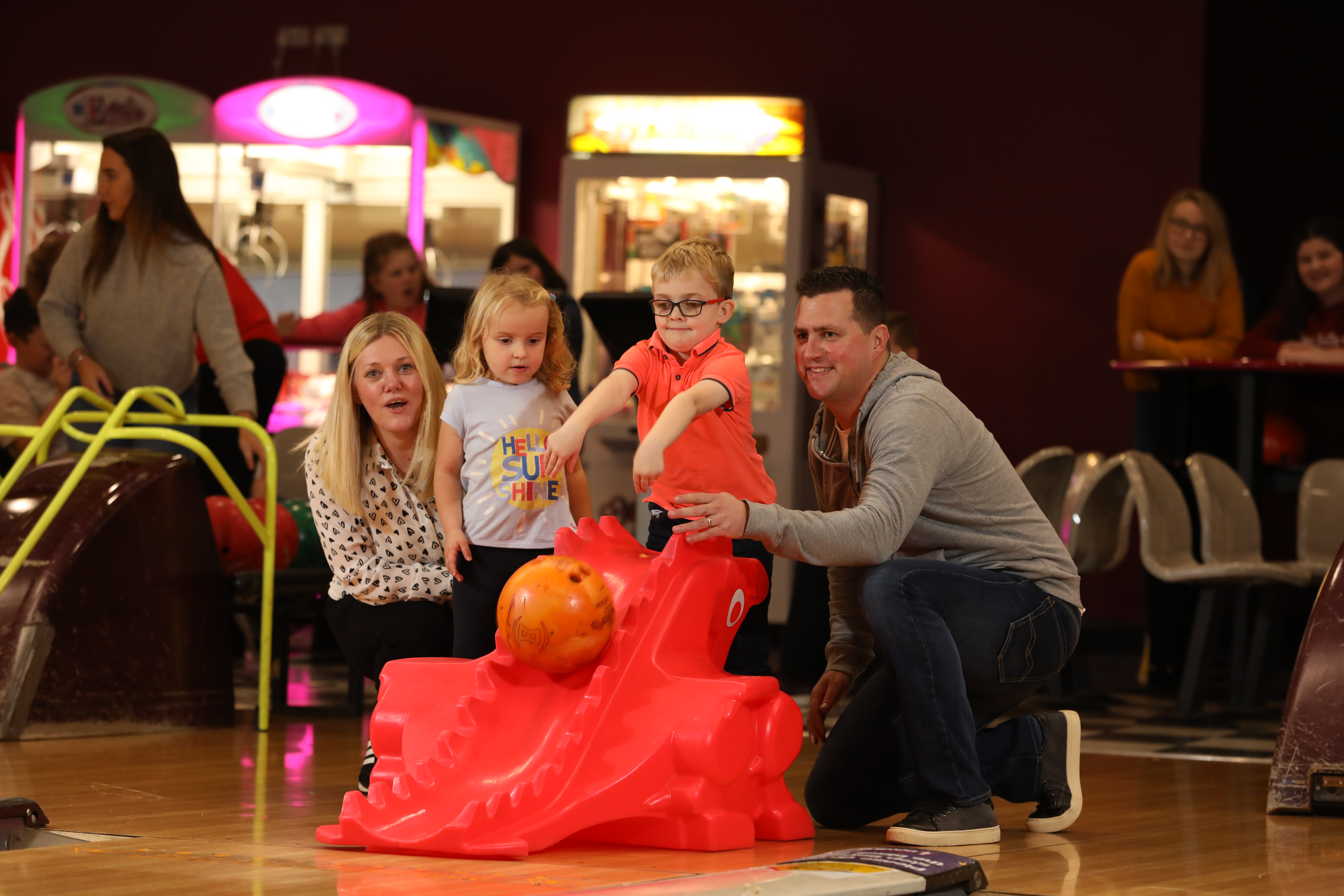 Family watch as little boy pushes bowling ball down kids tenpin bowling aid