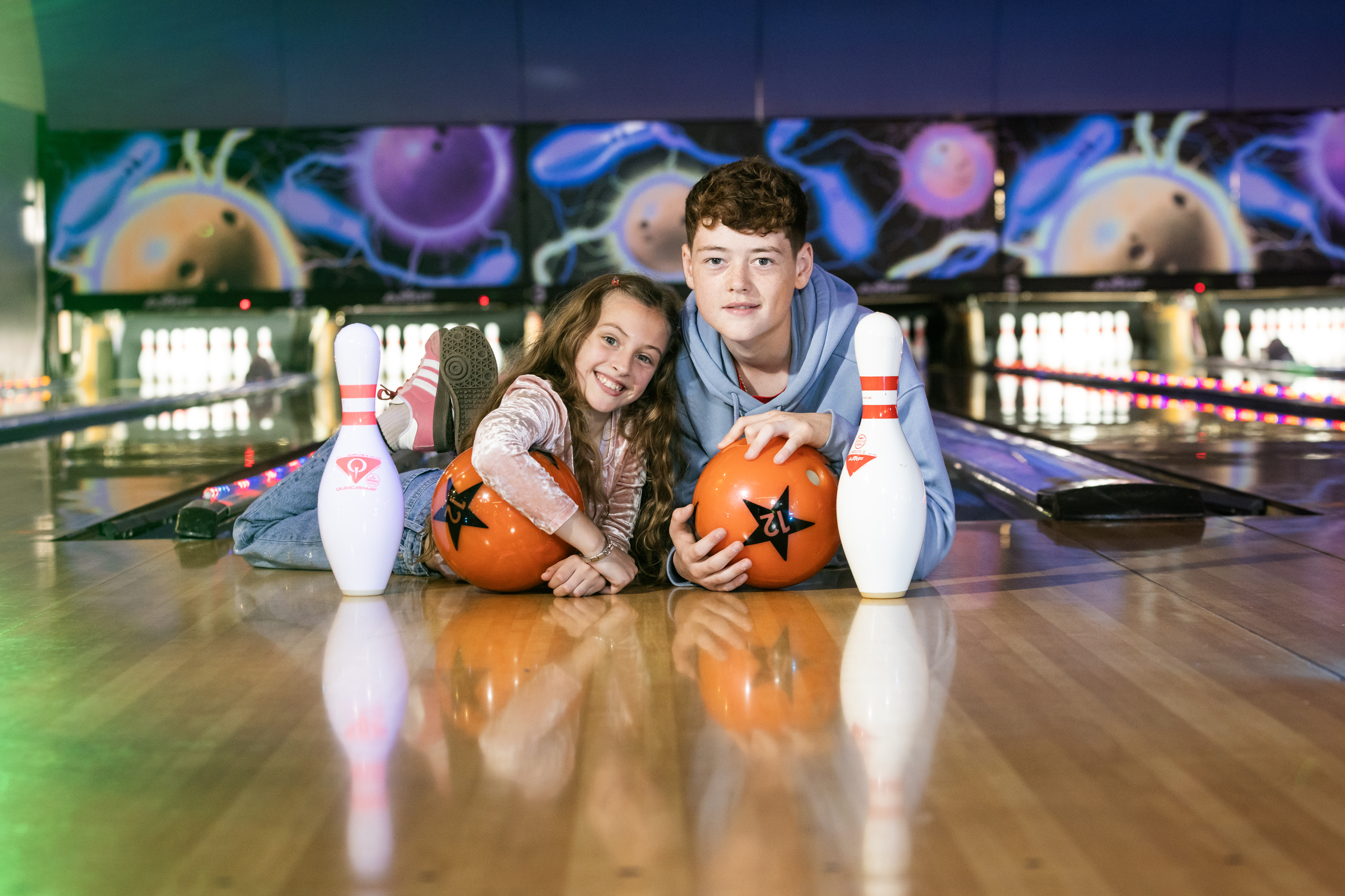 Family watch as little boy pushes bowling ball down kids tenpin bowling aid