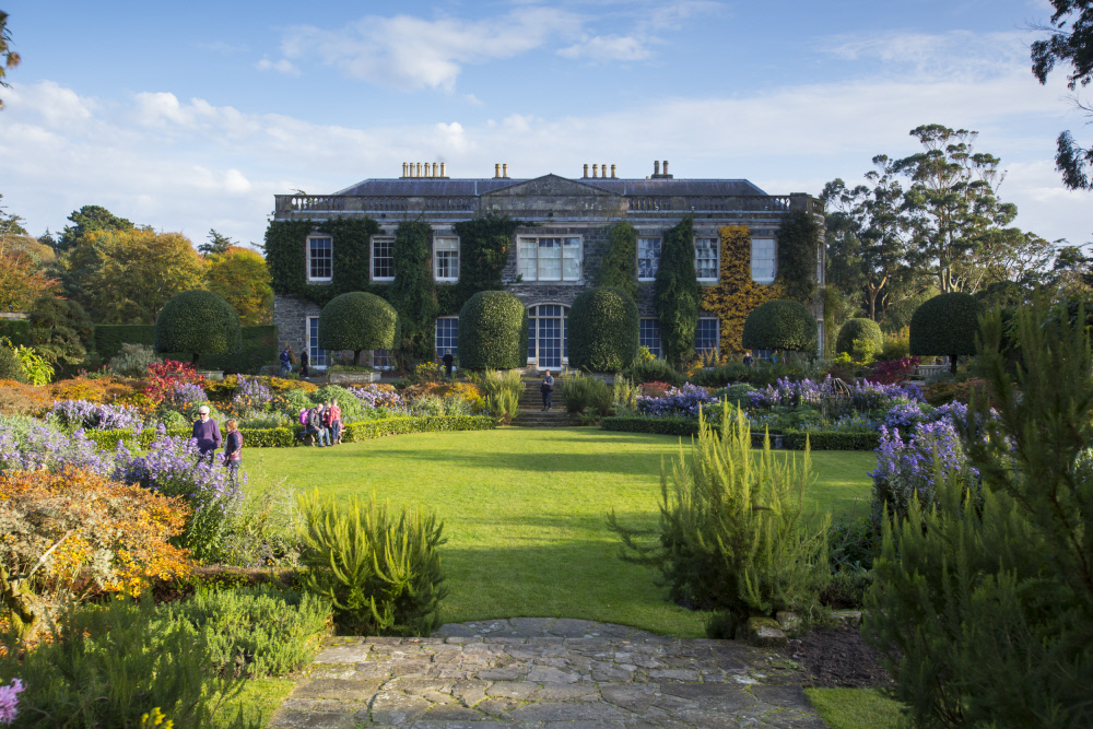 Victorian style mansion covered in ivy with big garden in foreground