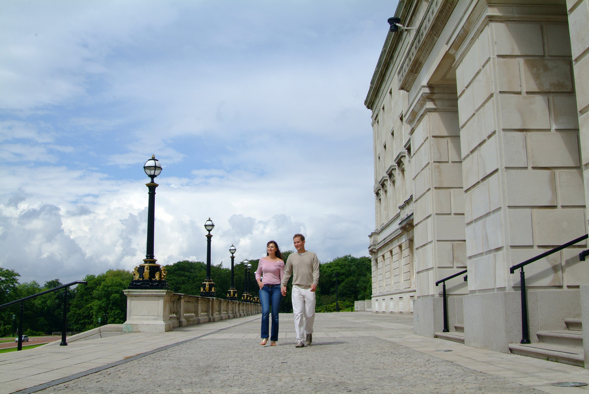 Man and woman walking in front of large white NI Parliament buildings