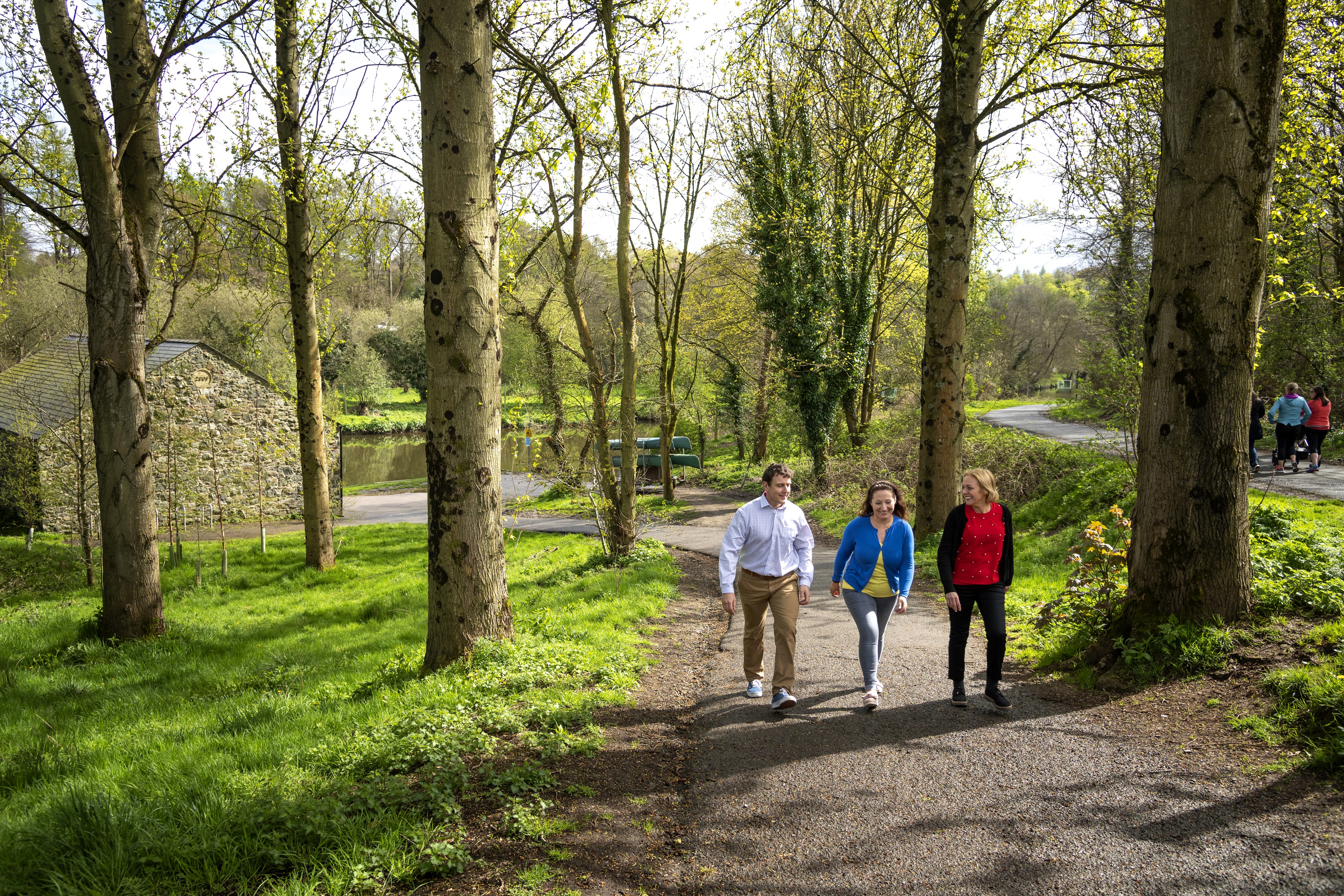 A man and two womwn walking along path with river in background