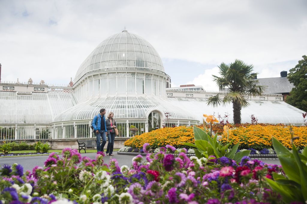 Man and woman walking in front of large glass greenhouse with lots of flowers in foreground